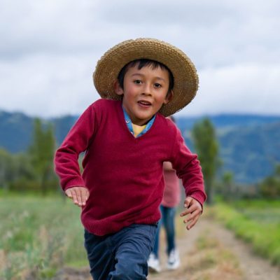 Happy Latin American boy playing outdoors at a farm and running on the road - lifestyle concepts